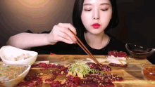 a woman is eating meat with chopsticks at a table