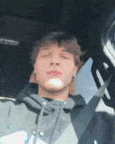 a young man in a hoodie is sitting in a car with his eyes closed
