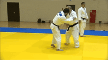 a man in a white kimono with a blue patch on the back is wrestling another man in a black belt