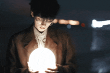a man wearing glasses is holding a glowing ball in his hands
