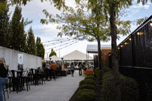 a fenced in area with tables and chairs and people walking around