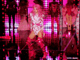 a woman with pink hair is dancing on a stage in front of a pink background