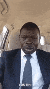 a man in a suit and tie is sitting in a car and making a funny face .