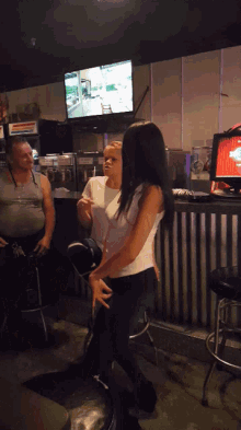 a woman in a white tank top is dancing in a bar with a man behind her