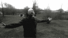 a person wearing a gas mask stands in a field with their arms outstretched