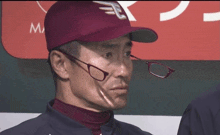 a man wearing glasses and a maroon baseball cap with the letter t on it