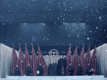 a group of people standing in front of a stage with red flags and a circle with a t on it
