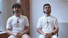 two men are sitting next to each other wearing white adidas shirts