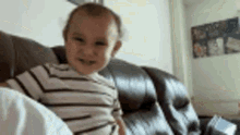 a baby is sitting on a couch looking at the camera and smiling .