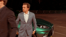 a man in a suit and tie stands in front of a green car