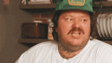 a man with a beard and mustache wearing a green hat and a white shirt .