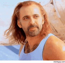 a man with a beard and long hair is wearing a blue tank top .