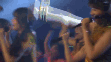 a blurry picture of a crowd of people with a woman holding a microphone in the foreground