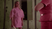 a woman in a pink dress is standing in a locker room talking to another woman .