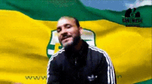 a man stands in front of a yellow and green flag with the words sabi music on it