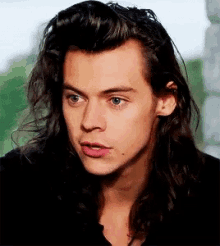 a close up of a man 's face with long hair and a black shirt .