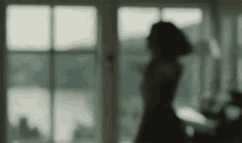a blurry picture of a woman standing in front of a window looking out .
