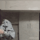 a woman is standing in a kitchen with white cabinets and a closet .