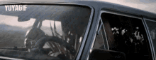 a man is driving a car with the word yuyagif on the bottom right corner .