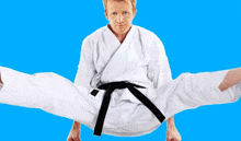 a man in a white karate uniform with a black belt is doing a split .