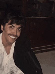 a man with a mustache and a white shirt smiles for the camera