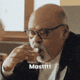 a man with glasses and a beard is drinking from a glass with the word masttt written below him