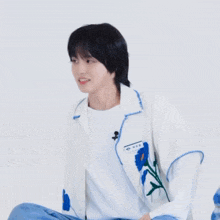 a young man wearing a white jacket with blue flowers on it