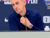 a man wearing a watch is sitting at a table with a microphone in front of a sign that says play