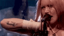 a woman with a tattoo on her wrist is singing into a microphone .