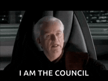 a man is sitting in a chair with the words i am the council on the screen behind him .