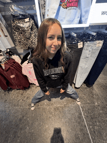 a girl wearing a black reebok hoodie stands in front of a display of clothing