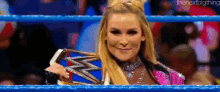a woman is standing in a wrestling ring holding a wrestling championship belt .