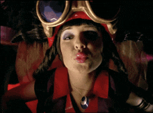 a woman wearing a red hat and goggles is blowing a kiss at the camera