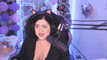 a woman wearing a cat ear headband sits in front of a microphone with balloons in the background
