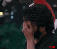 a man with a beard is covering his face with his hand and the word xhk is on the bottom