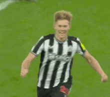 a soccer player in a black and white striped shirt is running on a field .
