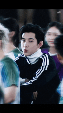 a man wearing a black adidas jacket stands in a crowd of people