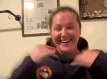 a woman in a blue sweatshirt is smiling and laughing in front of a framed picture on the wall .