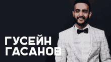 a man in a suit and bow tie stands in front of a black background that says guseih gasahob