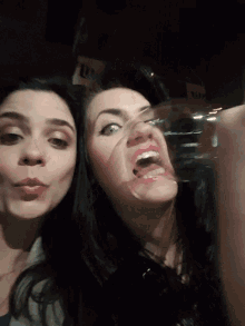 two women are making funny faces and one is holding a glass in front of her face