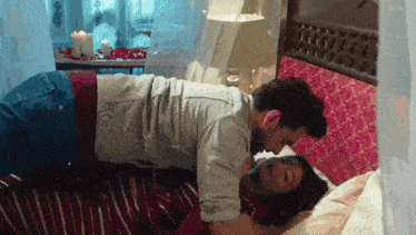 a man and woman are kissing on a bed with candles in the background .