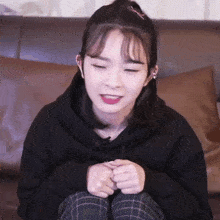 a girl in a black hoodie is sitting on a couch with her eyes closed