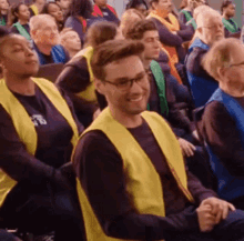a group of people are sitting in a room wearing yellow vests and smiling .
