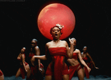 a woman in a red dress is dancing in front of a red moon .