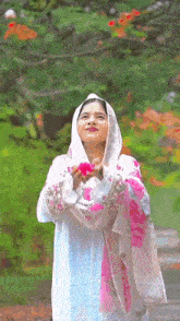 a woman in a white and pink dress is holding a pink flower in her hands .