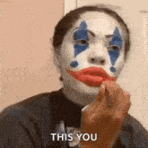 a woman is wearing a clown makeup and applying red lipstick to her lips .