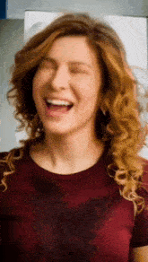 a woman in a red shirt is laughing with her eyes closed and her mouth open .