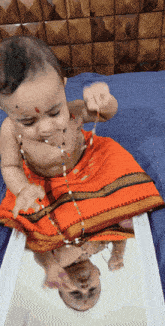 a baby in a red skirt is playing with a necklace in front of a mirror