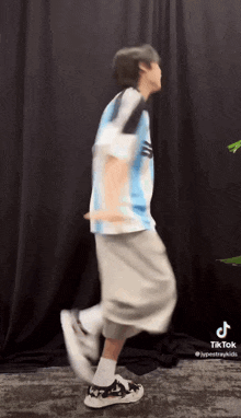 a man is dancing in front of a black curtain while wearing a blue shirt and grey shorts .