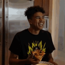 a young man in a black t-shirt is eating a slice of pizza .